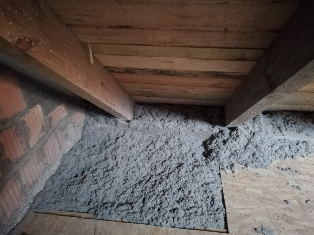 Podłoga na poddaszu z widocznym ocieplaniem celulozą pomiędzy drewnianymi belkami.